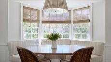 Everhem x Annie Meyers-Shyer collaboration wooden woven window blinds show here in a curved bay window with a built in breakfast nook, gingham pendant light, and striped upholstery