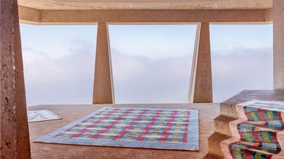 colourful rugs on a dusty floor, view out a window behind