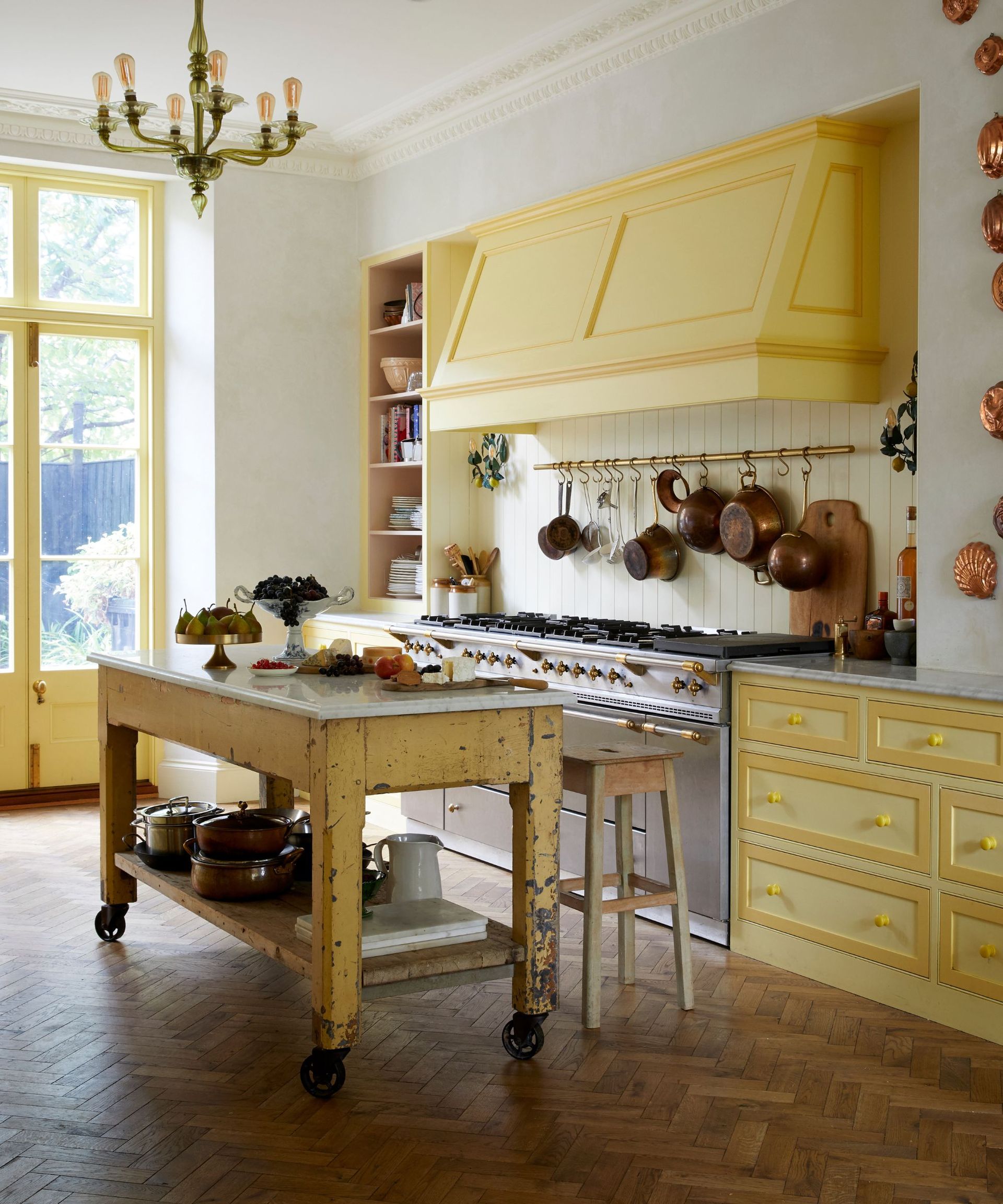 yellow vintage kitchen with a rustic yellow kitchen island and a large range cooker hood with antique copper accessories