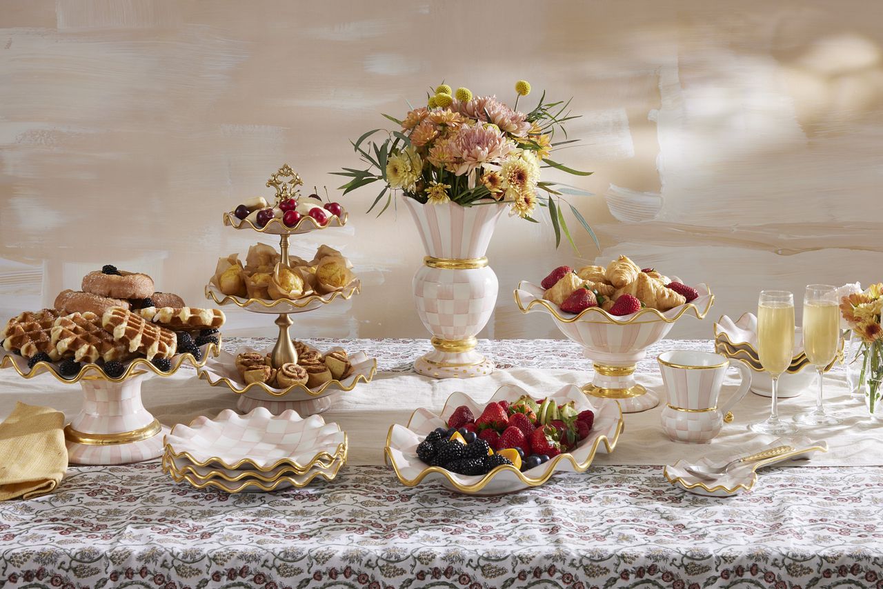 Elegant table setting with a selection of pink and white checkered dinnerware with gold trim. The collection is filled with pastries and fruit