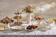 Elegant table setting with a selection of pink and white checkered dinnerware with gold trim. The collection is filled with pastries and fruit