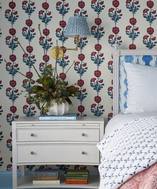 bedroom with blue and white floral wallpaper, white nightstand, blue wall sconce and blue and white headboard with white bedding and patterned throw blanket