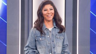 Julie Chen Moonves smiling on the Big Brother stage in a denim shirt.