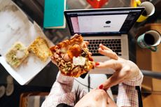 Woman eating pizza in the kitchen over laptop