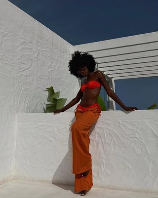 Woman wearing orange bikini top and orange pants.