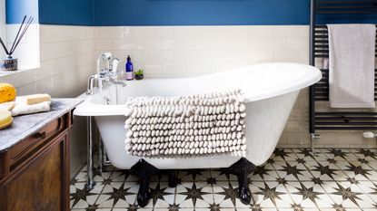 Roll top bath in a bathroom with dark blue walls and white tiles and a black and white patterned tiled floor