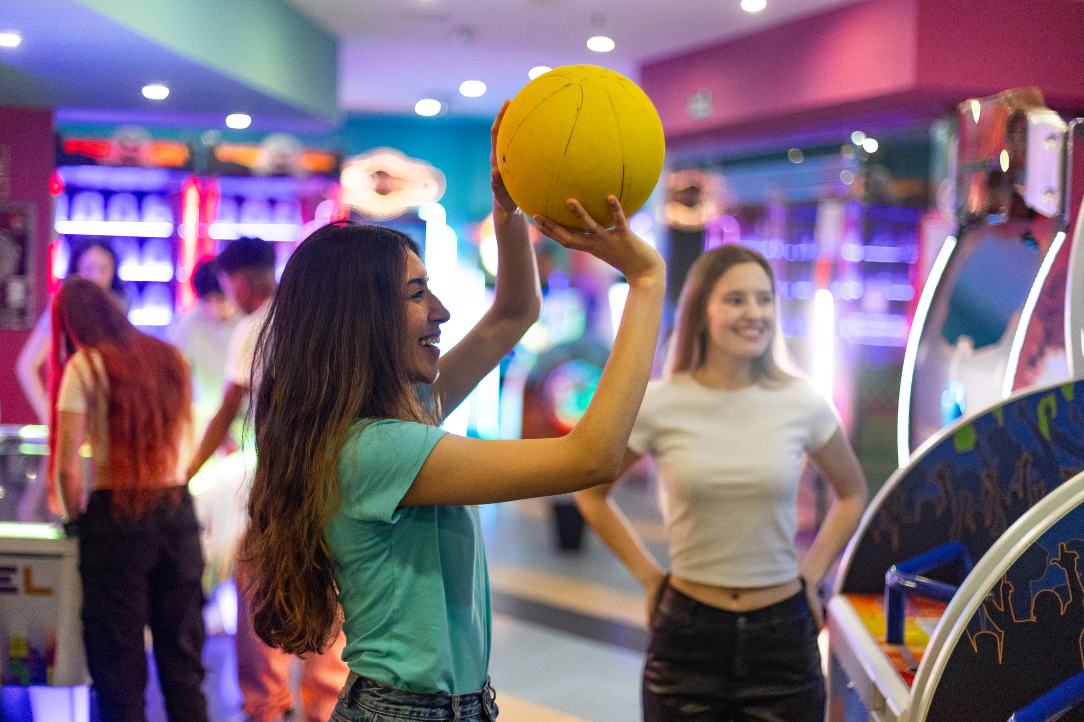 Two friends enjoying their time together while playing a vibrant basketball arcade game, sharing laughter and creating joyful memories indoors