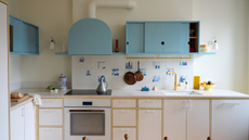 a small kitchen with a delft tile backsplash, blue upper cabinets and white lower cabinetry