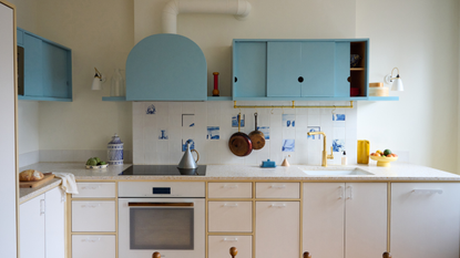 a small kitchen with a delft tile backsplash, blue upper cabinets and white lower cabinetry