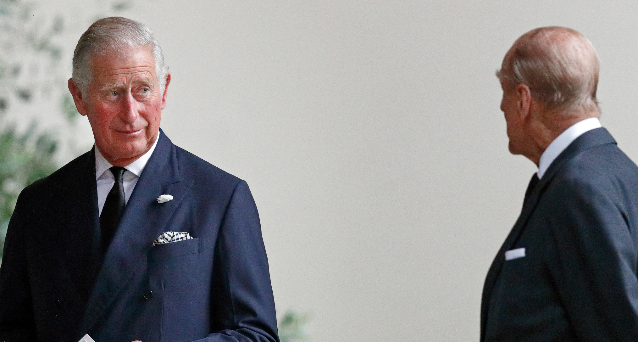 Prince Charles holding a paper and turning to look at Prince Philip