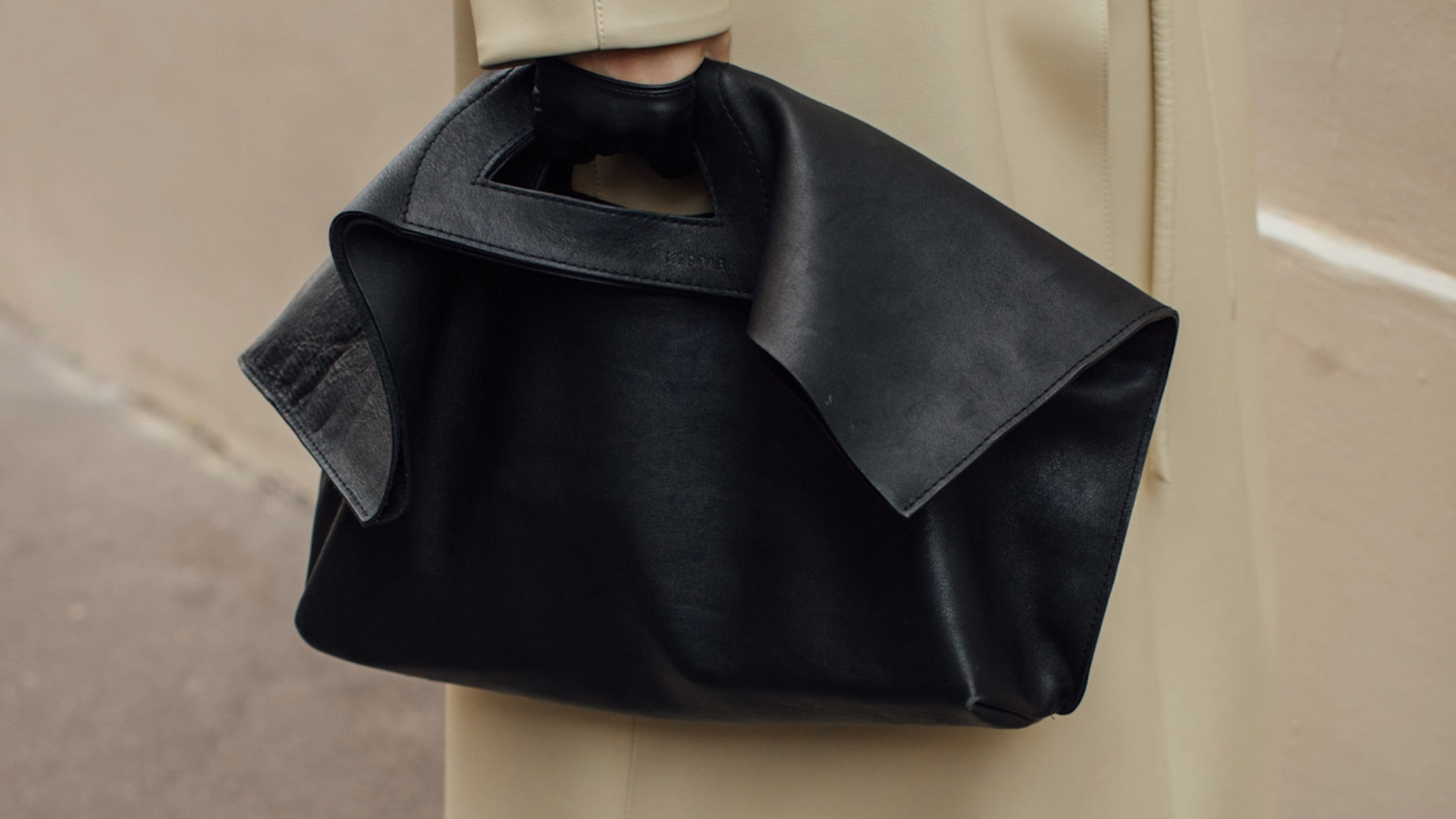 woman carrying a black shoulder bag with a trench coat. 