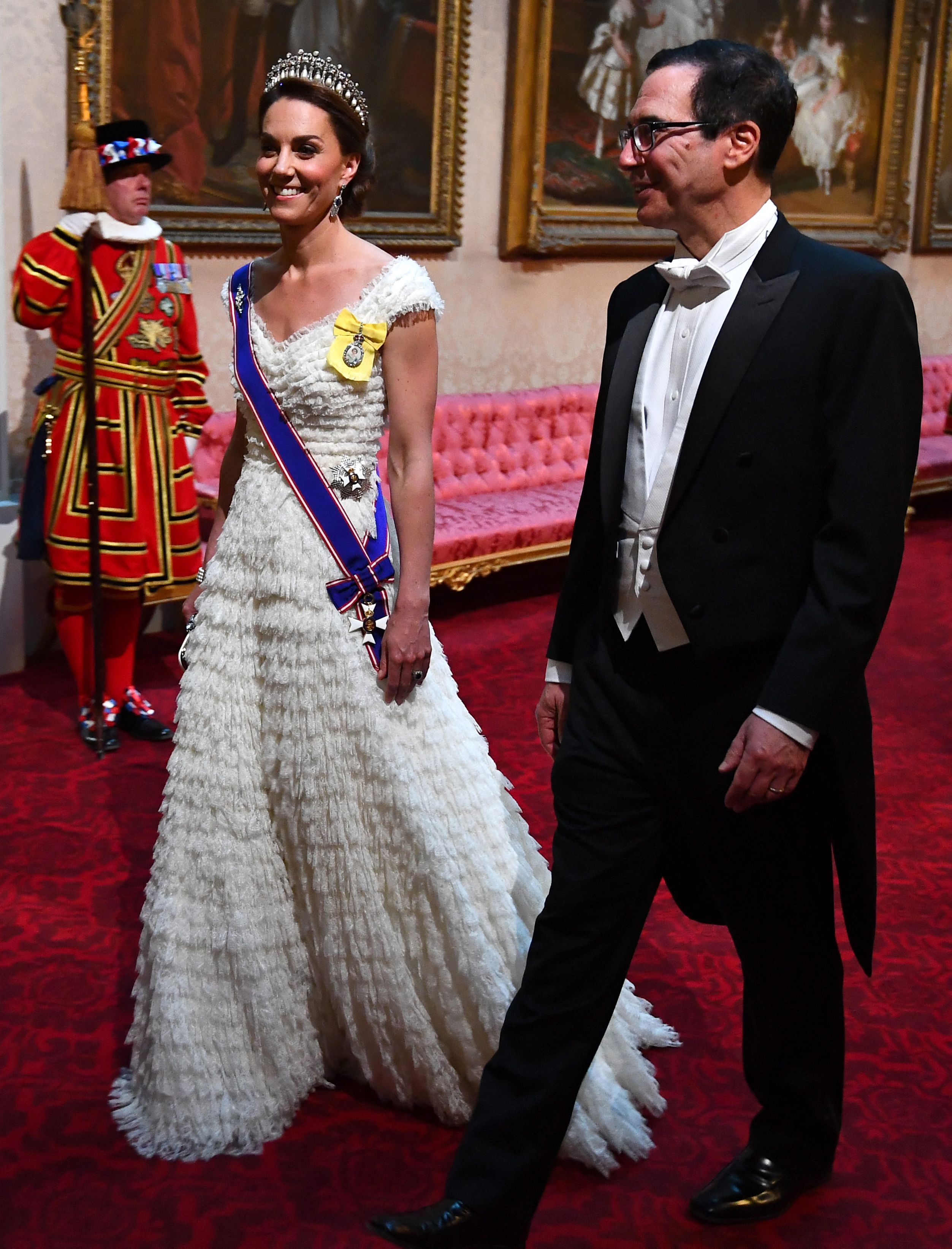 Kate Middleton wearing a white gown and tiara walking next to a man in a tux