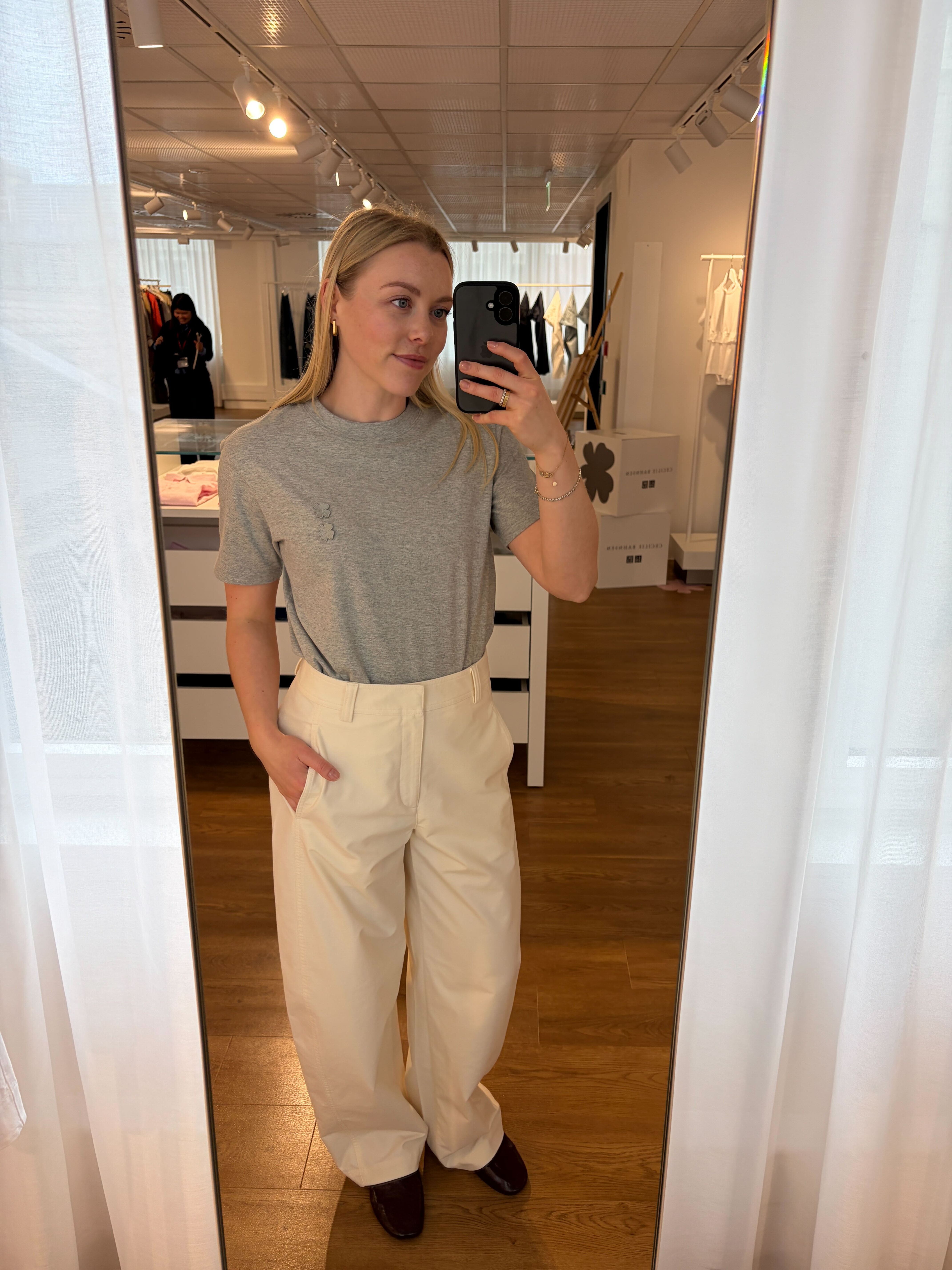 Florrie is wearing a gray tee and cream trousers
