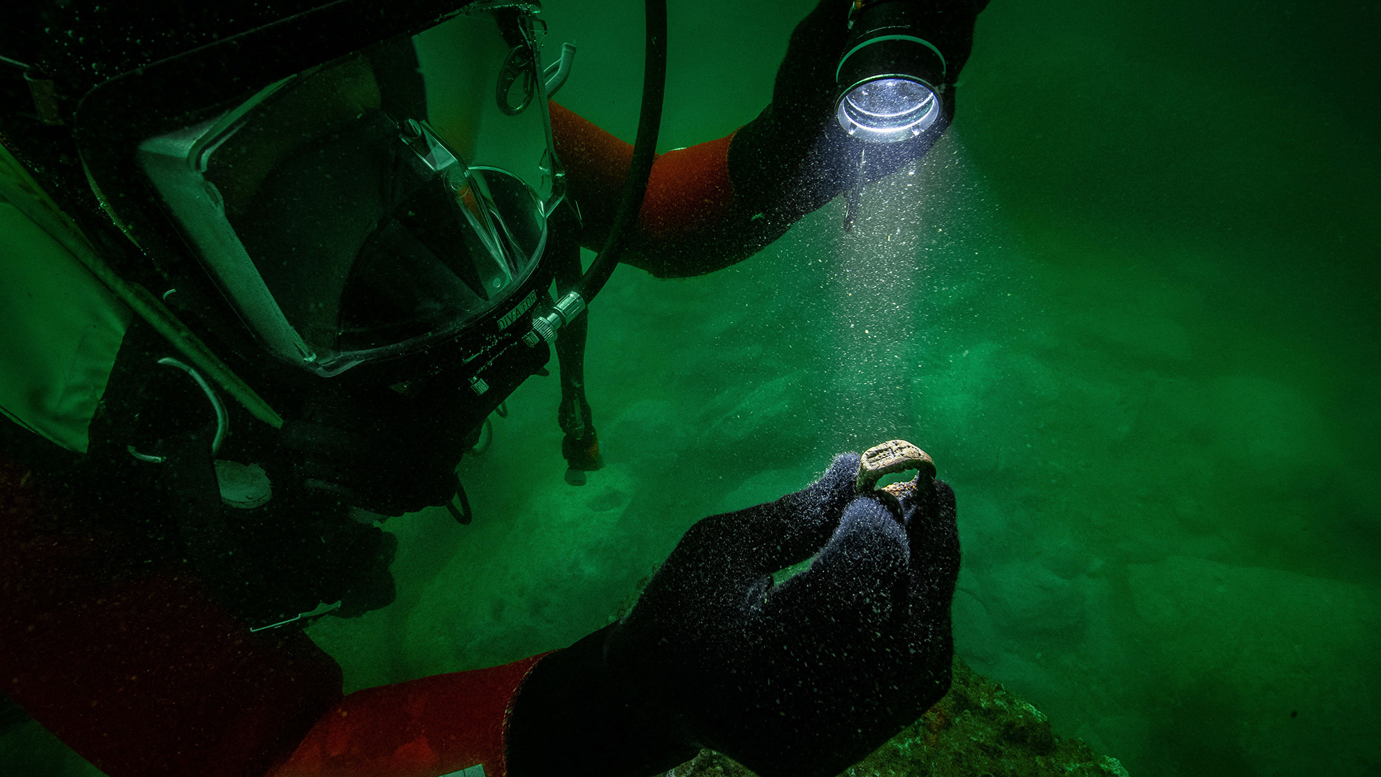 An underwater image of a diver holding up a small ring under a flashlight.