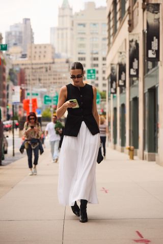 woman wearing a black button-down vest and white skirt and black boots at new york fashion week