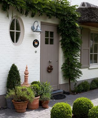 A white brick house with a mushroom colored front door with a small wreath on it