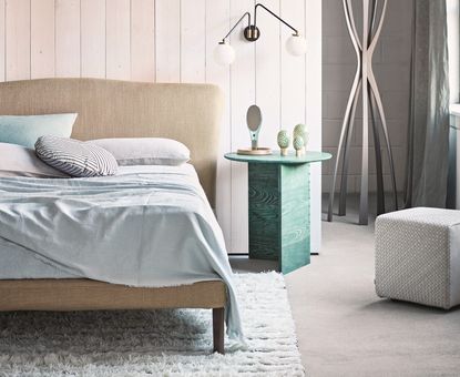 Bedroom with polished concrete floor, double bed with pale green bedding, green bedside table and cushion and pale wood panel 