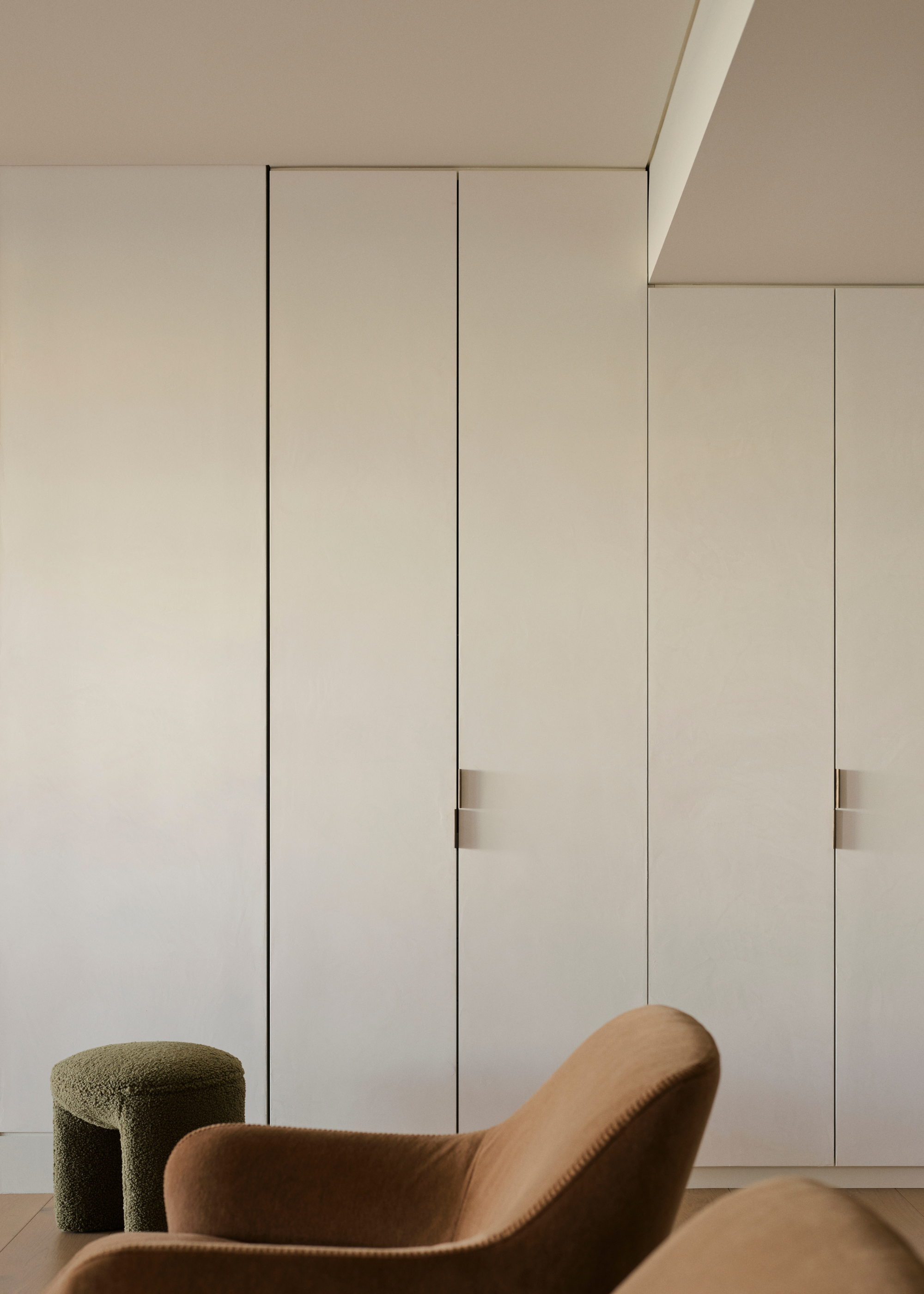 A white closet with a deep green pouf and a brown sofa chair