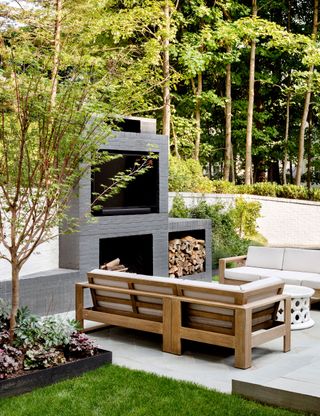 outdoor seating space with white sofas and contemporary pizza oven with wall and mature trees around