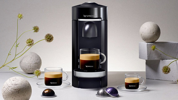 The Nespresso Vertuo Plus surrounded by coffee and Vertuo capsules