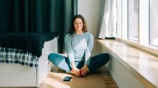 Woman sits on yoga mat with the soles of her feet pressed together and a smartphone in front of her on the mat