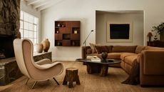 neutral cozy modern layered living room with a seagrass rug, large corner sofa in a toffee color upholstery, wooden vintage coffee table and large stone fireplace