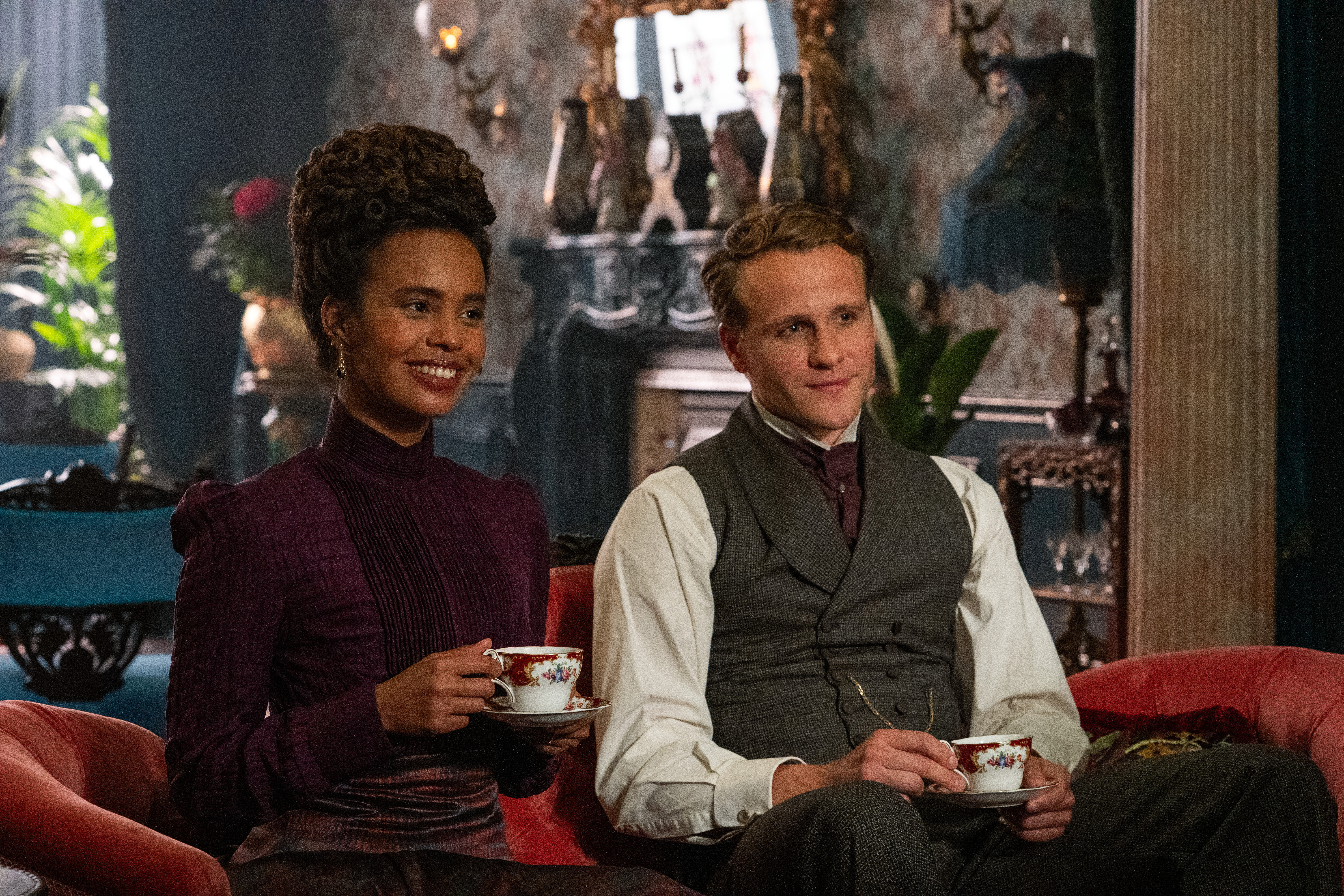 alisha boe and josh dylan in the buccaneers season 2 sitting on a couch having tea