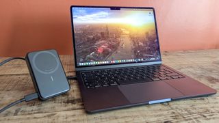 Anker MagGo Power Bank connected to MacBook Air next to each other on wooden table with orange wall in background