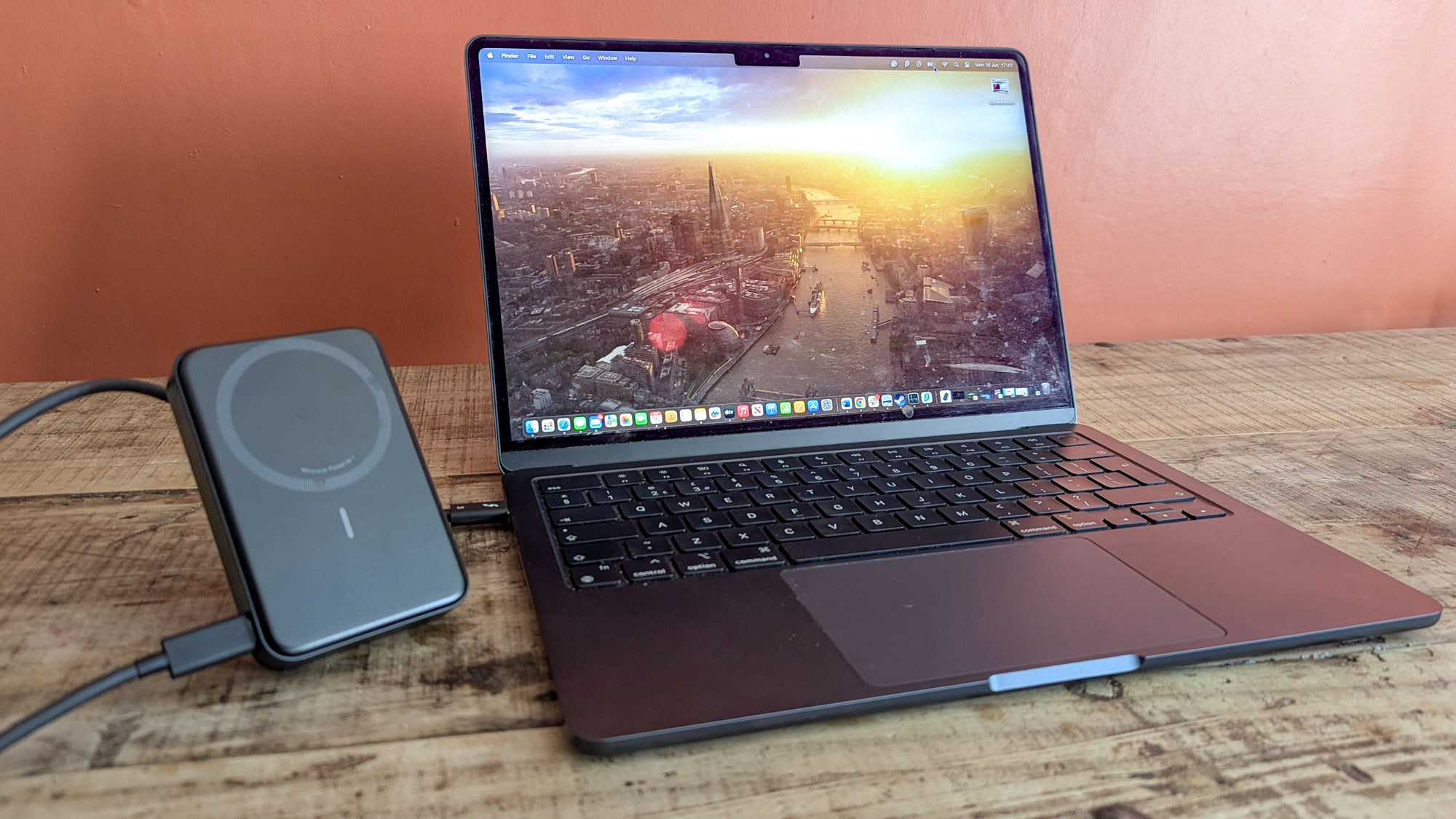 Anker MagGo Power Bank connected to MacBook Air next to each other on wooden table with orange wall in background 