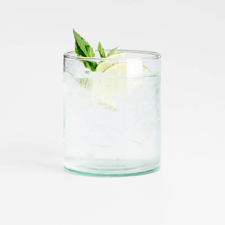 A green-tinted old fashioned drinking glass with a mint leaf