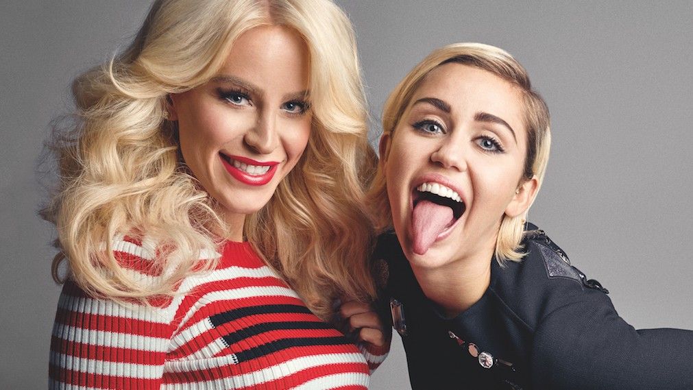 Smiling Gigi Gorgeous in red and white and Miley Cyrus in black pulling tongue