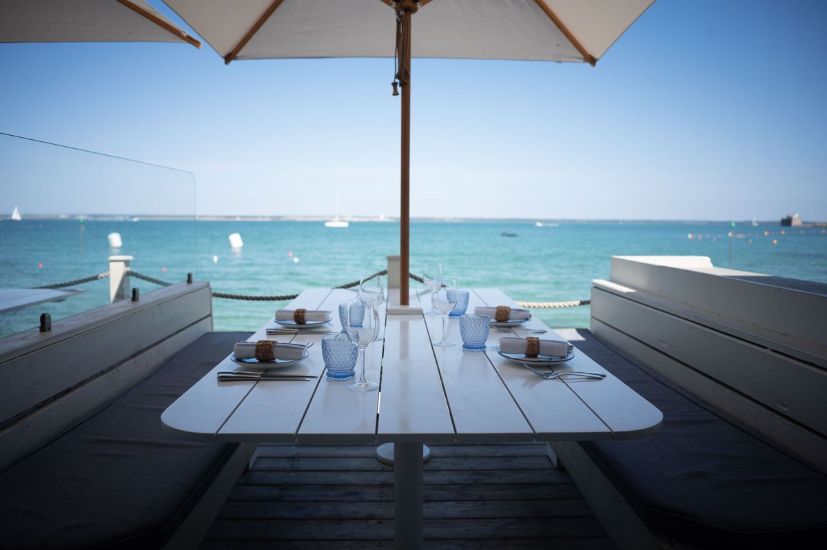 Beachside restaurant table laid and ready for customers, shaded by umbrella, on a sunny day