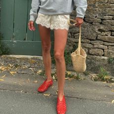 Woman in lace shorts, gray sweatshirt, and red jelly shoes