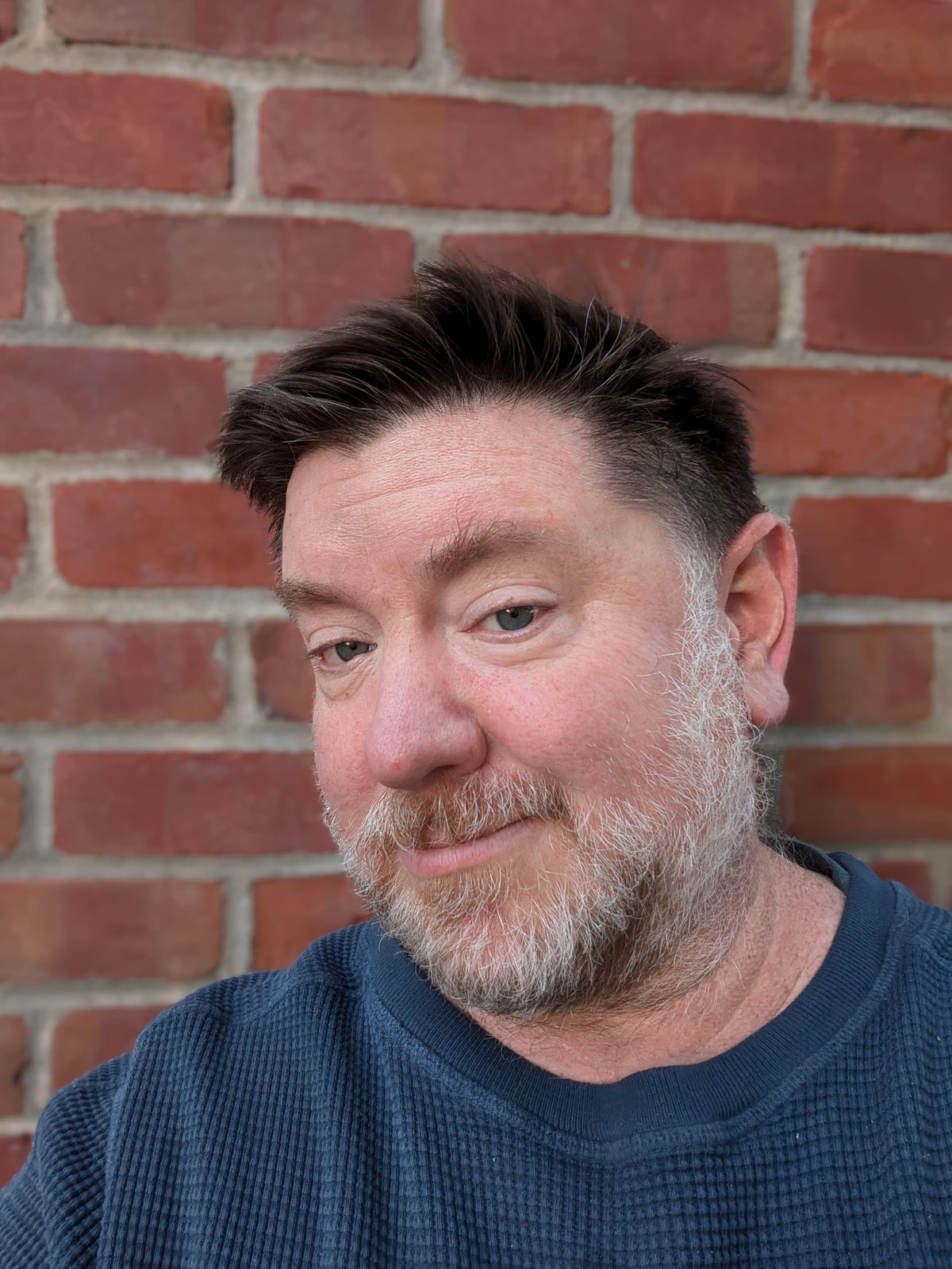 Selfie taken in portrait mode in front of a brick wall by the Pixel 8a