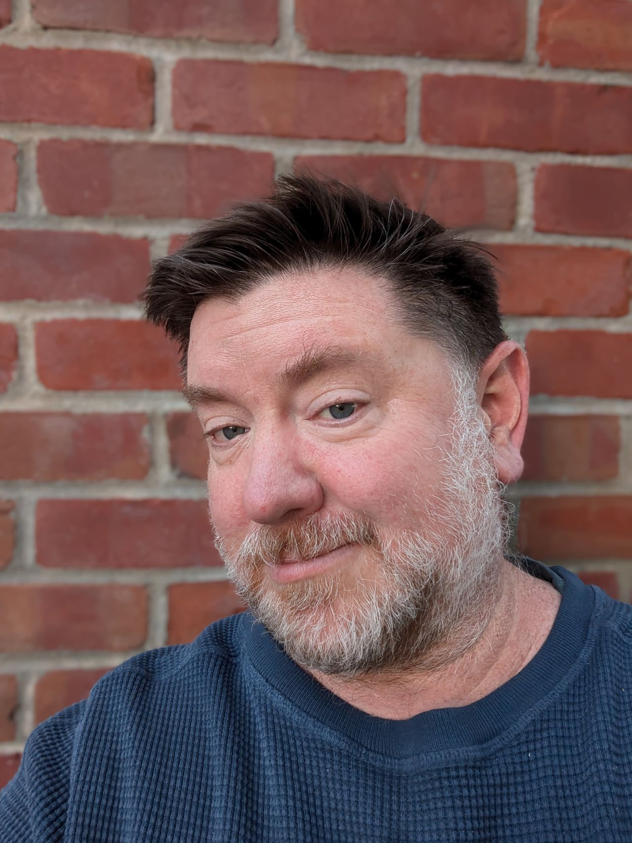 Selfie taken in portrait mode in front of a brick wall by the Pixel 8a