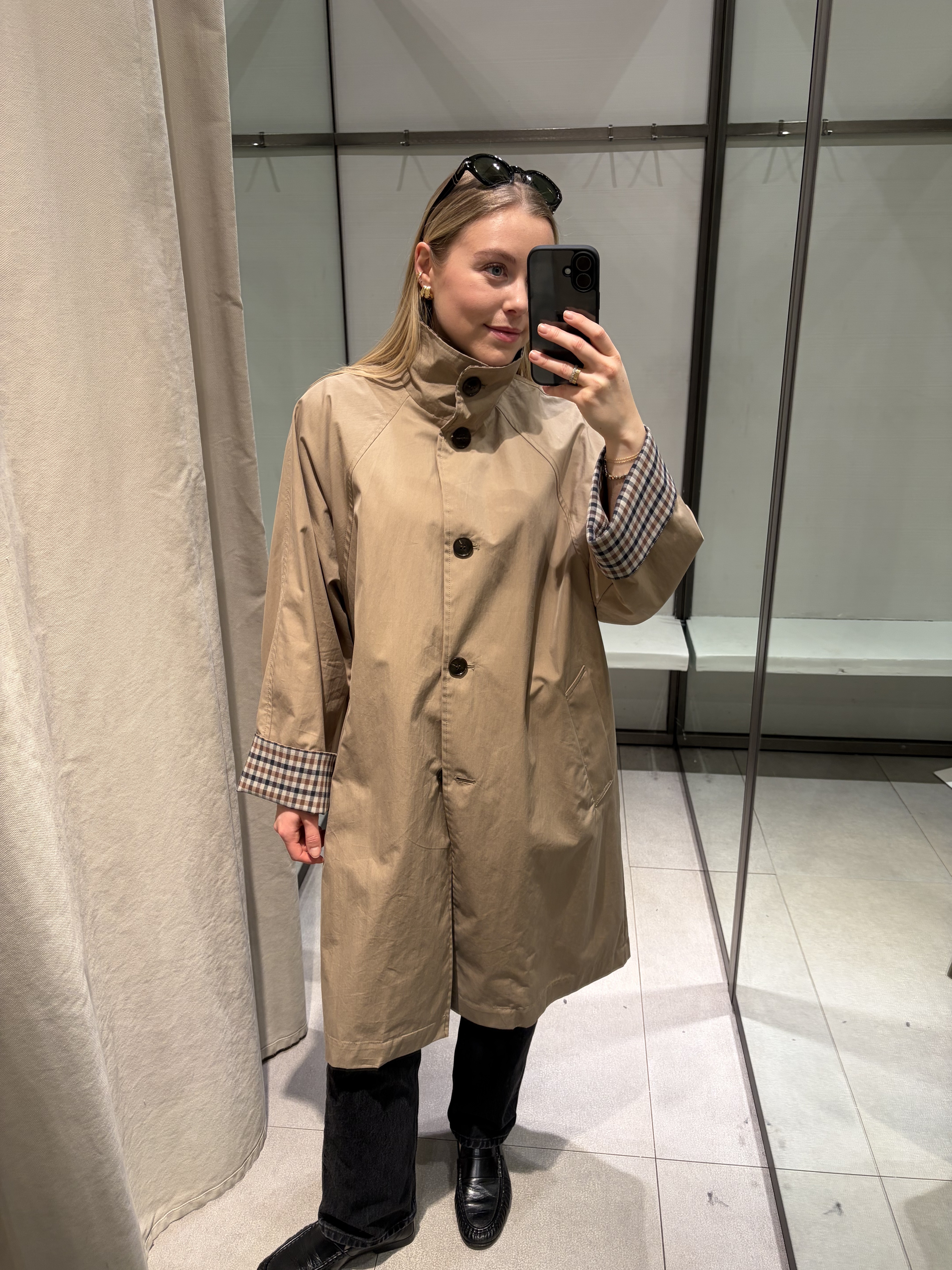 Woman wears beige trench coat with check cuffs, black jeans and black loafers