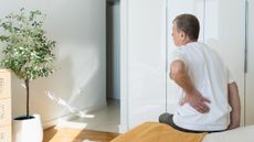 Person sitting on edge of bed, holding lower back