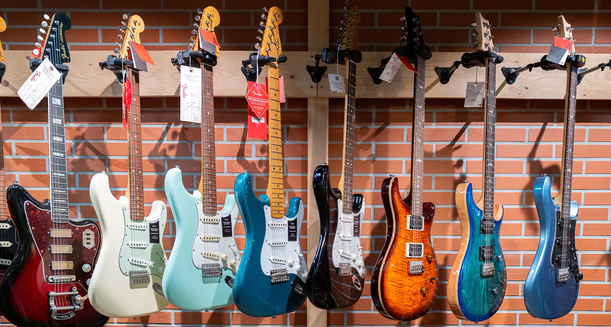 A photo of Fender and PRS Guitars handing on a wall rack at a guitar store.