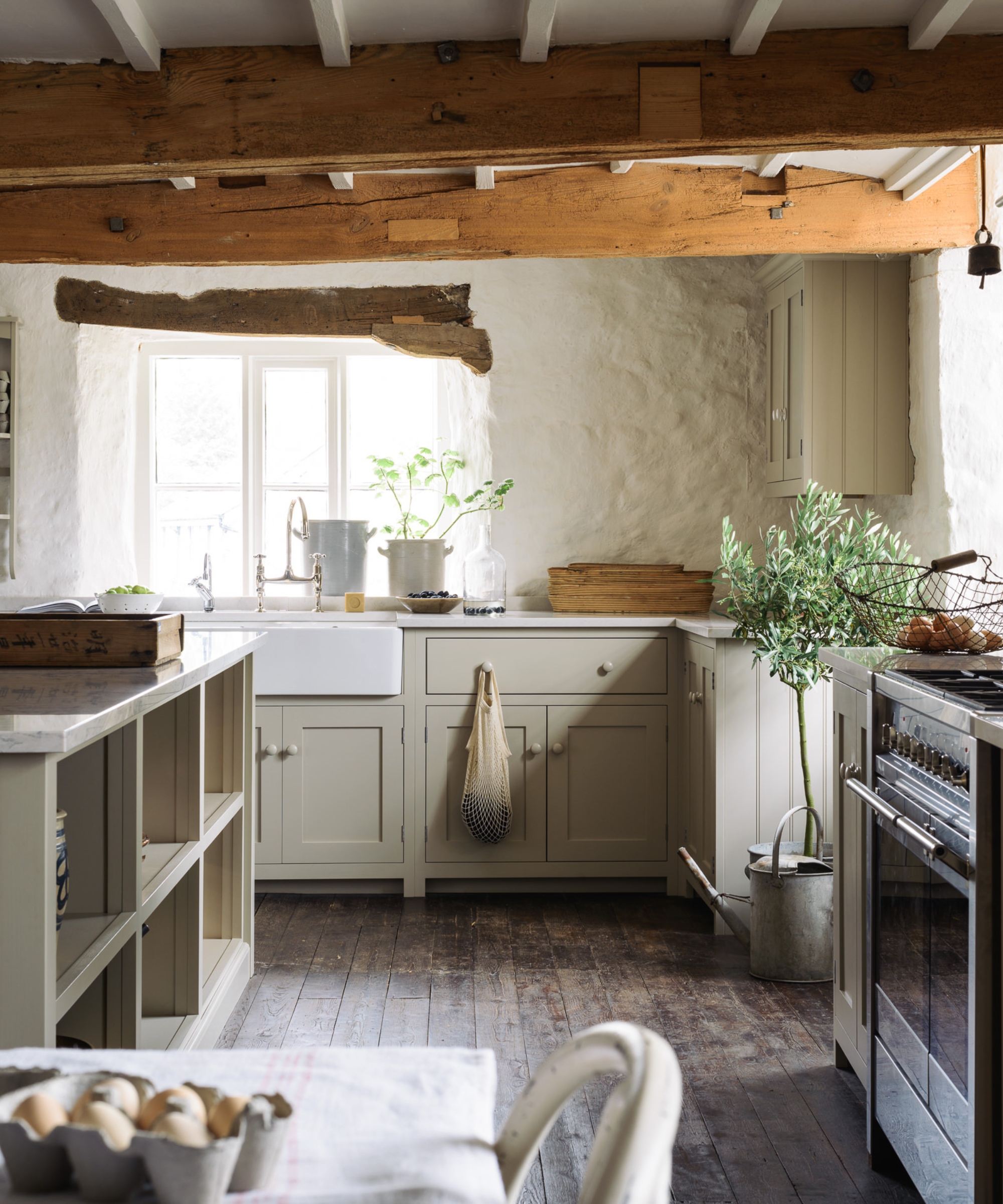 A country kitchen with mushroom color cabinets, white walls, and dark wood floors