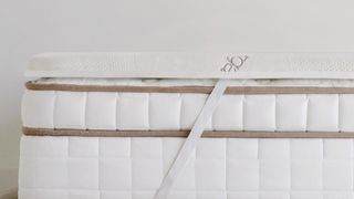 Image shows the Saatva Mattress Topper Latex placed on a cream mattress to make it feel firmer