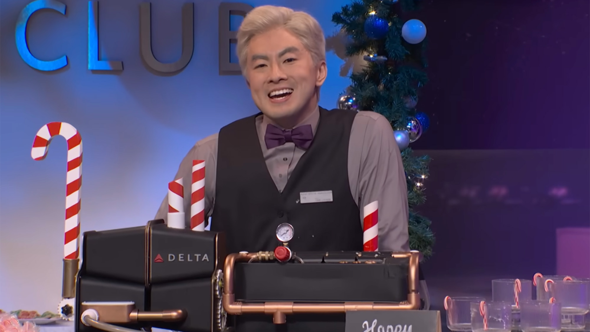Bown Yang stands in the airport club in "Delta Lounge," his final SNL sketch. He has on a button down, vest and purple bow tie.