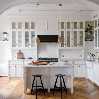 Fitted white country kitchen through period archway with kitchen island and brass fittings on parquet floor