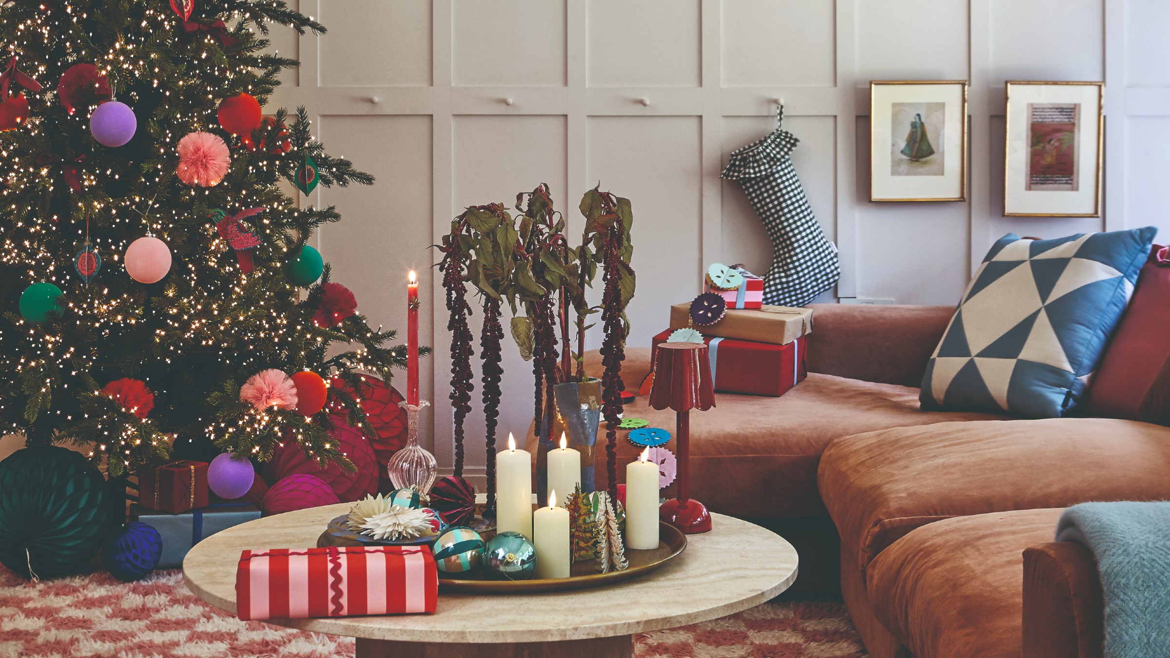 A living room with a brown chaise sofa decorated for Christmas with a lit-up Christmas tree, presents and a Christmas stocking 
