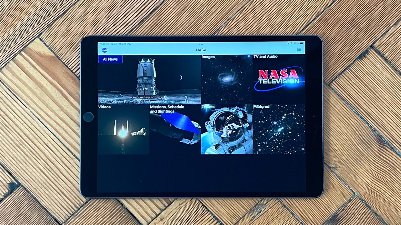The main home screen on the NASA app as displayed on an iPad laying on herring bone wooden flooring