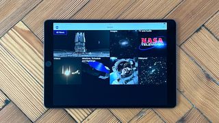 The main home screen on the NASA app as displayed on an iPad laying on herring bone wooden flooring