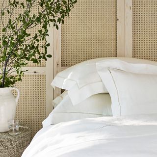 White pillows stacked on a bed against a wicker panelled wall