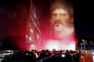 Fans light flares as they gather under a mural depicting Diego Maradona in Naples