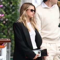 Sofia Richie and Elliot Grainge walk hand in hand after dinner at Cipriani in Beverly Hills on April 26, 2025. Richie is wearing a black coat, white T-shirt, black bottoms, and red Proenza Schouler net heels.