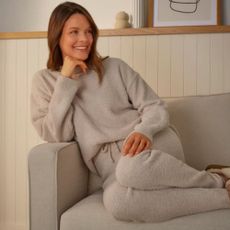 Middle aged woman wearing fluffy neutral pyjamas on a beige settee