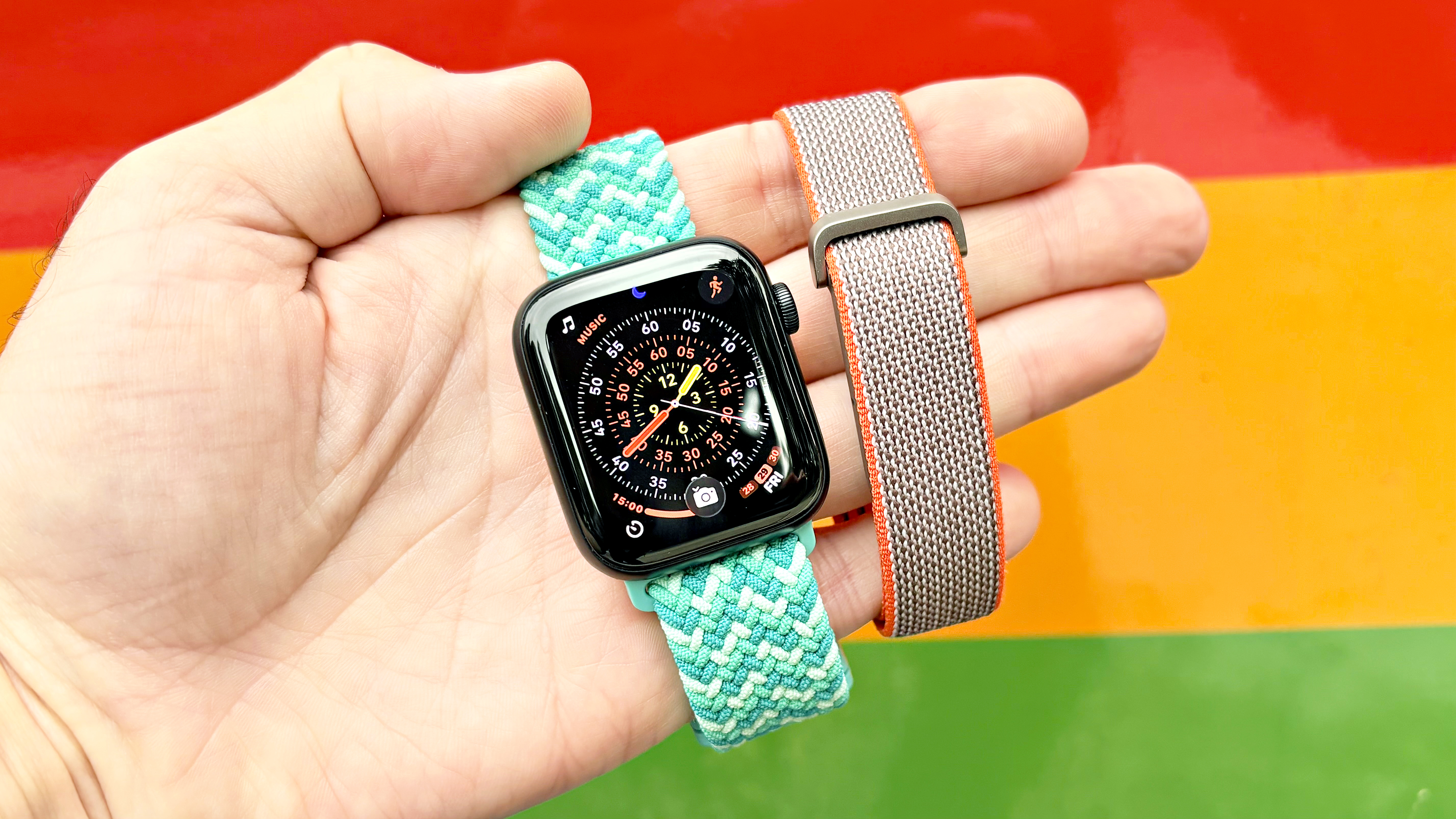 Close-up of the Apple Watch SE 3 and Fitbit Air in a user's hand against a colorful, vibrant background